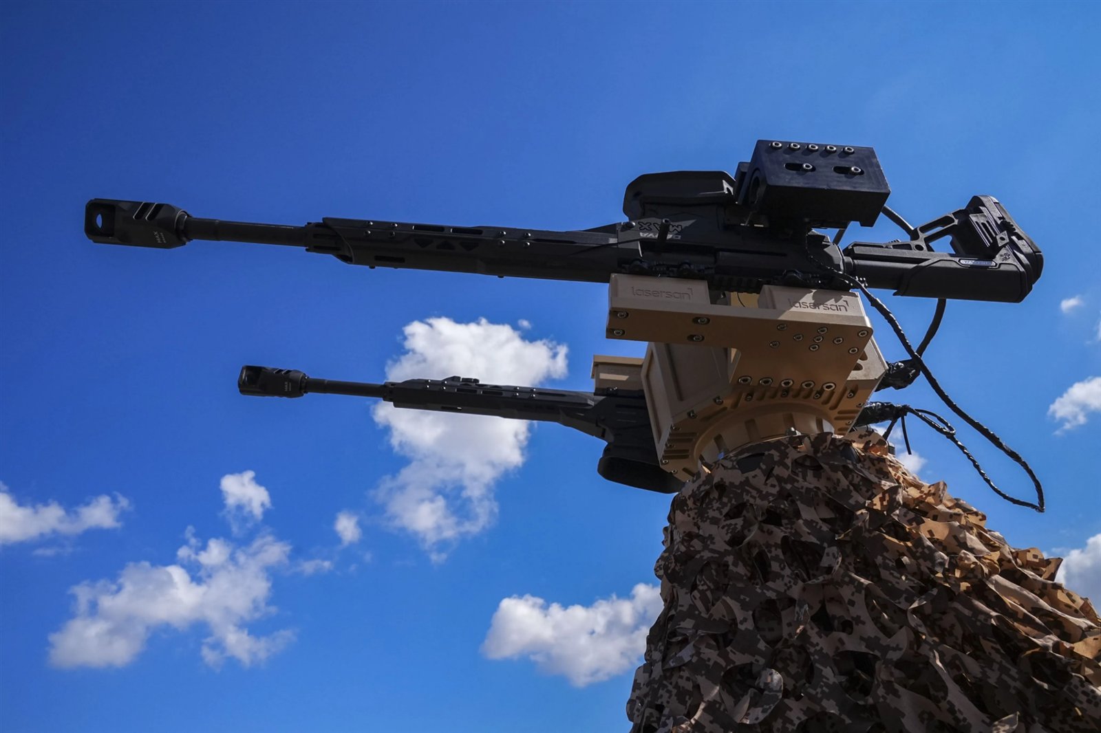 Dron Kalkanı kulesi Boran-8 saha testinde: kamuflaj ağıyla örtülü araç üzerinde, mavi gökyüzüne doğru çevrilmiş iki yarı otomatik tüfek ve Lasersan elektro-optik sensör kutusu.